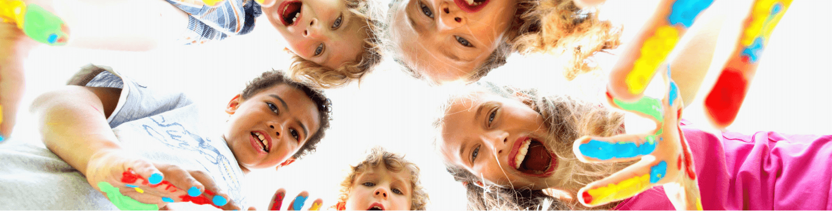 Fröhliche Kinder mit bunten, bemalten Fingern schauen lachend in die Kamera. Die Aufnahme ist von unten gemacht, sodass die Kinder im Kreis stehen und nach unten schauen.