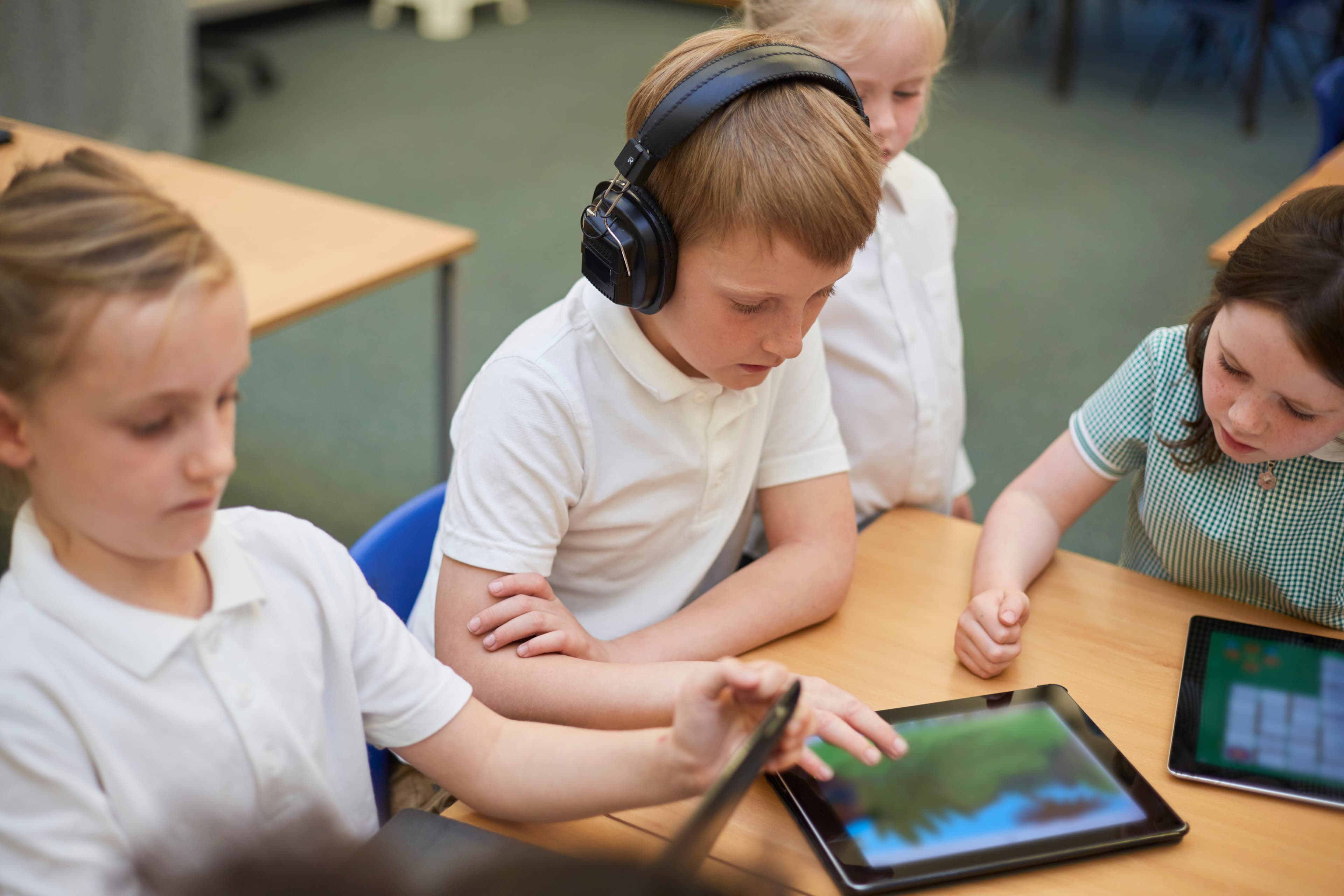 Grundschulkinder lösen gemeinsam digitale Sprachrätsel auf Tablets im Unterricht